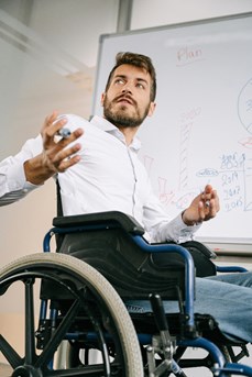 Un travailleur en chaise roulante devant un tableau blanc durant une présentation